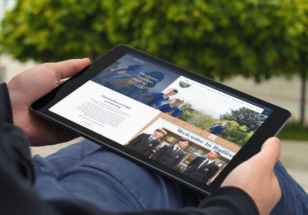 A tablet held by hands in the sunshine, showing Rutlish homepage