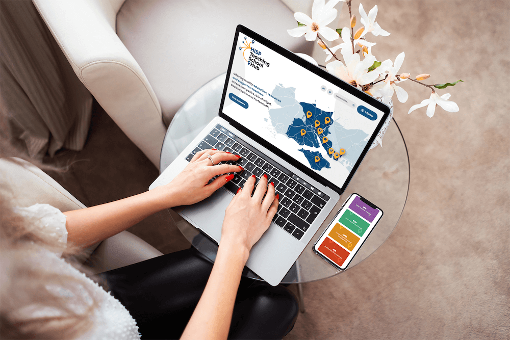 HISP website on laptop - showing map illustration with phone on glass table and flowers behind.